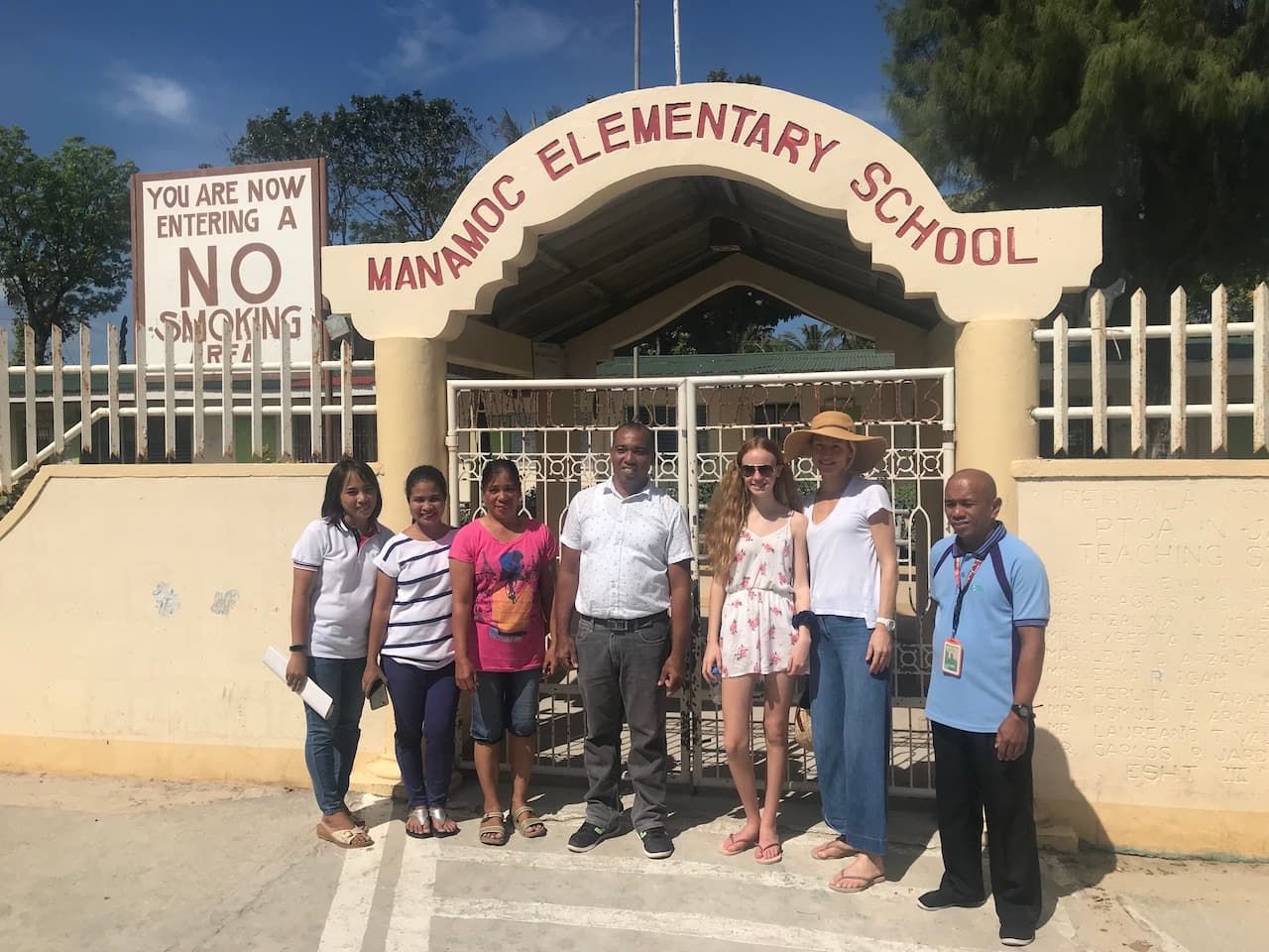 Natalia standing outside Manamoc Elementary School with staff members