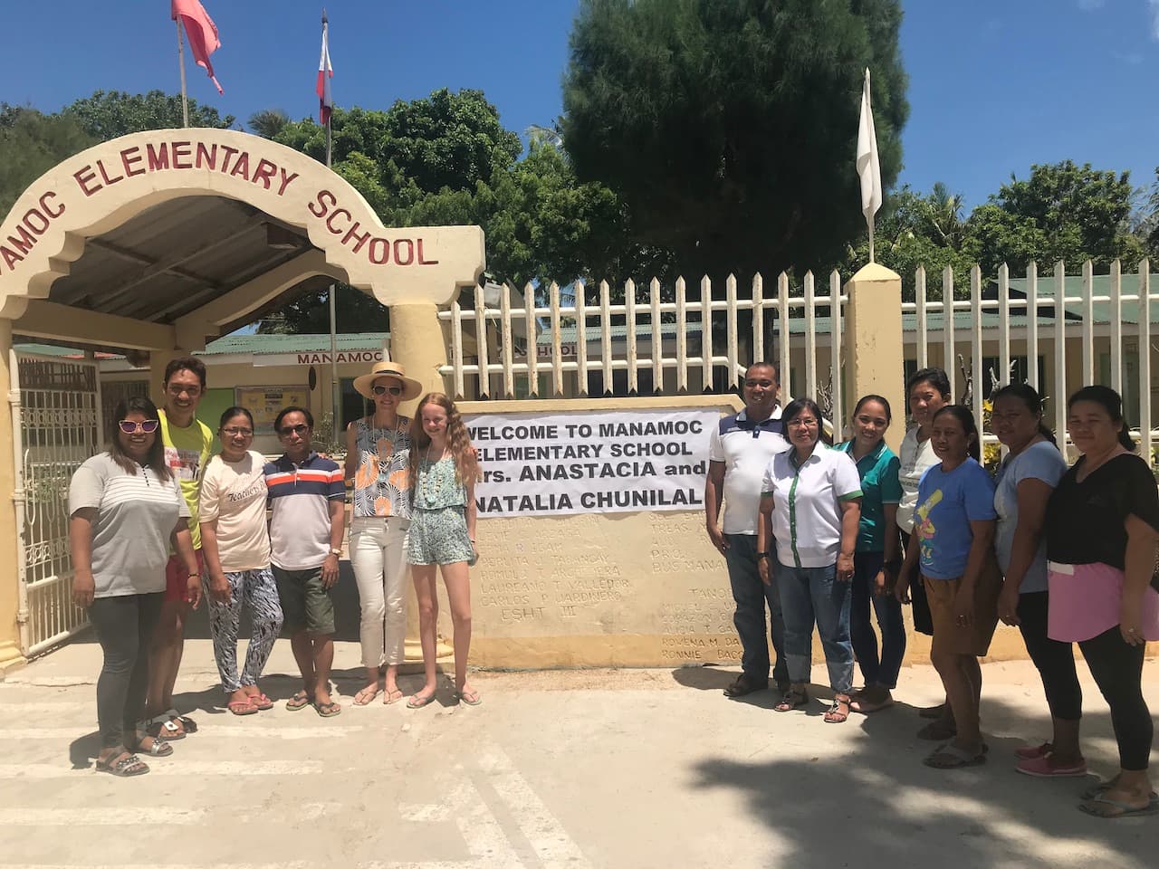 Natalia standing outside Manamoc Elementary School with staff members